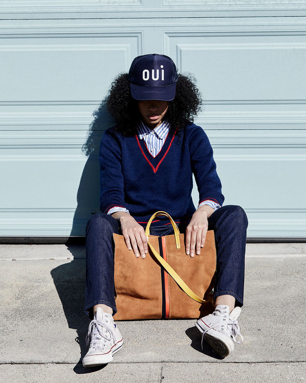 Bree is seated on the sidewalk wearing the Navy Oui Trucker hat