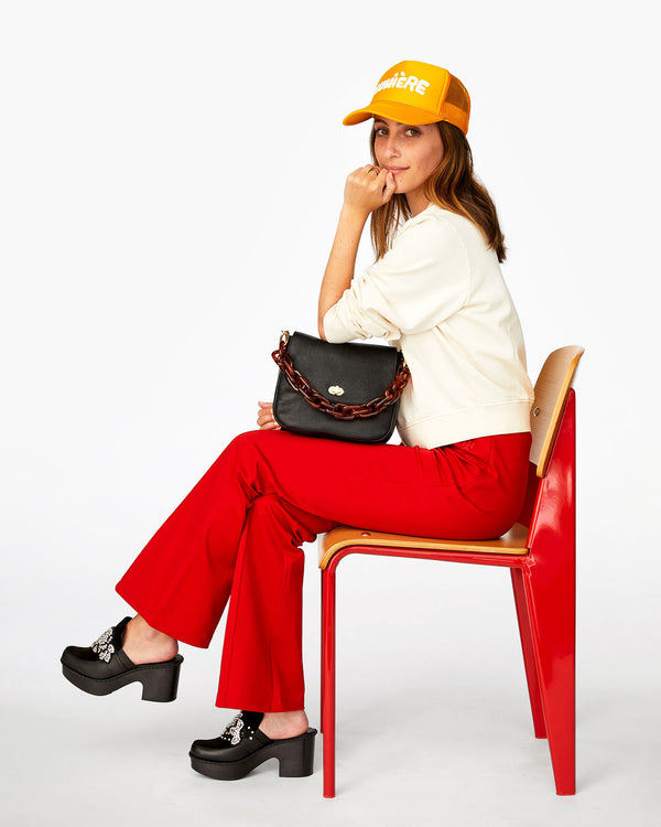 Frannie sitting in a chair with the Black Turnlock Louis on her lap with the tortoise  resin shortie strap