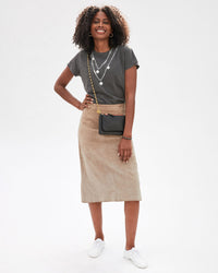 mecca in white sneakers, a tan skirt and a faded black tee with the Brass Box Chain Crossbody Strap on the black wallet clutch plus