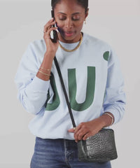Mecca wearing the Loden Croco Midi Sac as a crossbody bag and putting her phone inside of it. 
